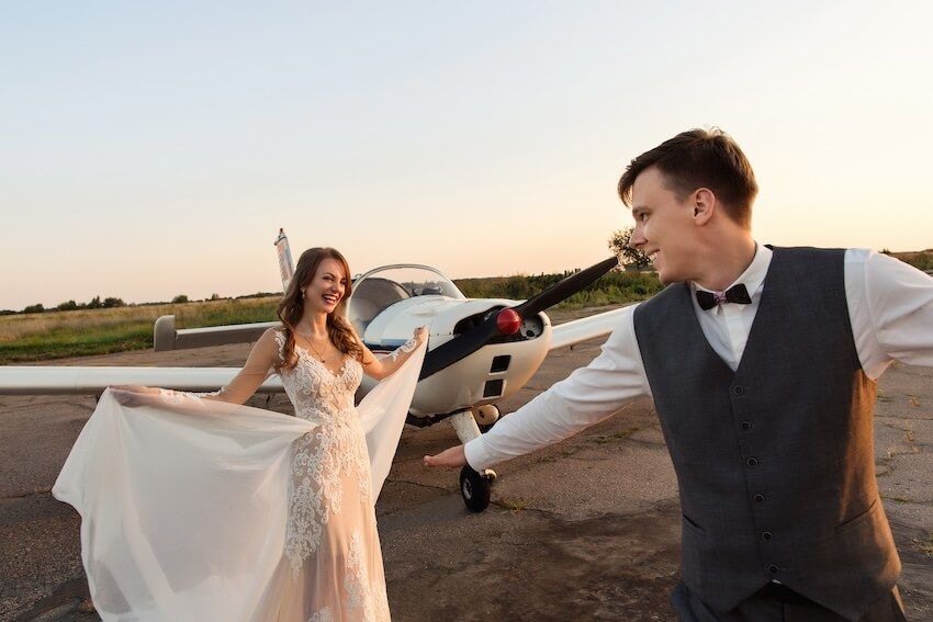 Passport wedding invitations: bride and groom dancing beside a small airplane