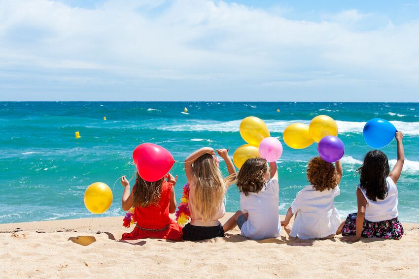 Beach birthday party: kids holding some balloons at a beach